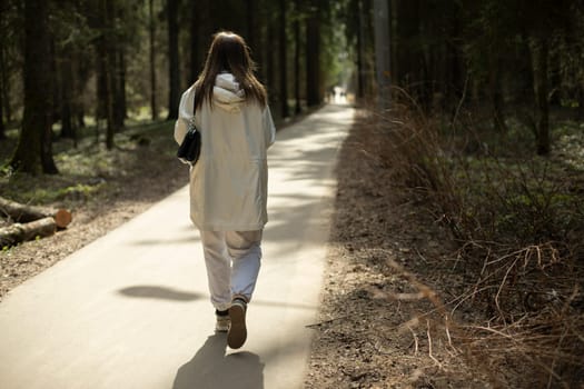 Girl in white clothes walks through park. Woman on long walkway. Modern style of clothing.
