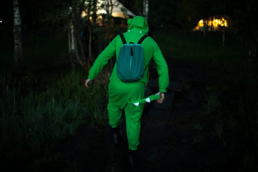 Man in green suit walks through woods. Guy in fun crocodile costume. Man at music festival in nature.