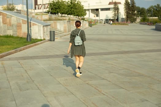 Girl walks through square in summer. Walk around city. Girl with small backpack. City is in summer.