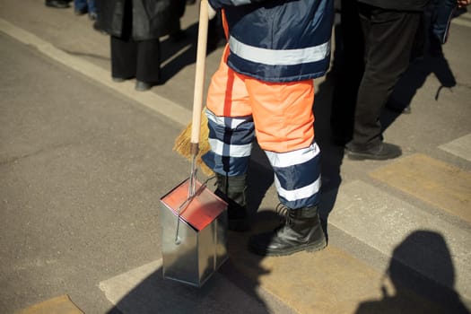 Janitor on street. Sweeping street. Garbage collection in city. Man in orange clothes.