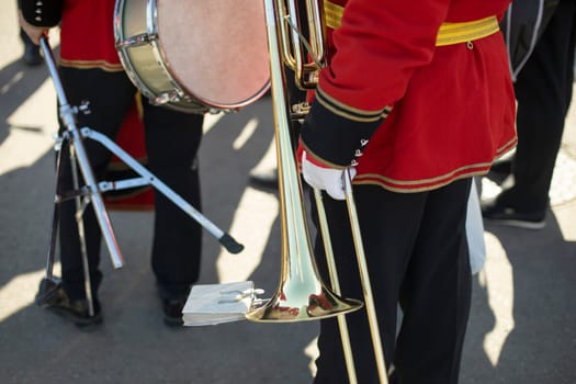 Orchestra member holds brass pipe. Trumpeter details. Ceremonial red uniform. Military band on street.