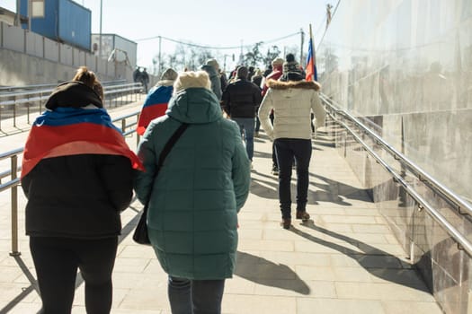 People walk around city in spring. Citizens on street. Lot of people from behind. Pedestrians walk through pedestrian zone.