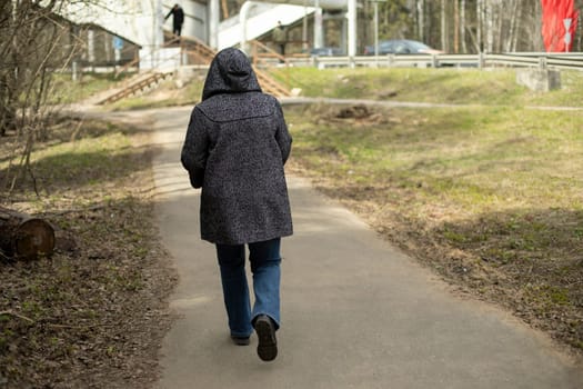 Woman in hooded jacket. Road in park. Woman walks along hiking trail.