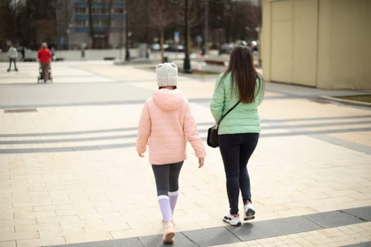 Two girls walk through square. Mother and daughter on street. Walking outside in summer. People in metropolis.