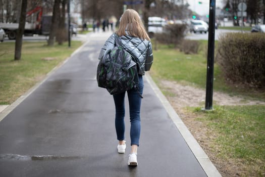 Woman walks through city. Girl in jeans on street. Backpack and jacket. Pedestrian road.