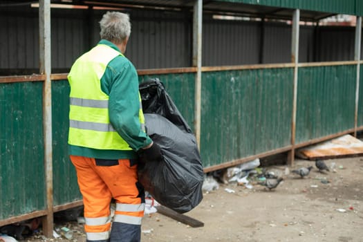 Janitor takes garbage to trash. Man throws out black bag.