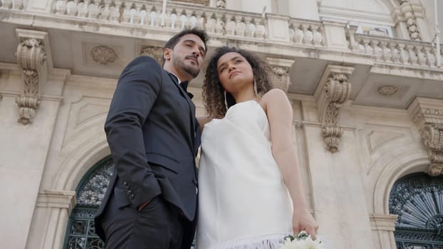 Wedding couples posing on the street. Action. Newlyweds in fashionable wedding costumes posing cute on the street in summer weather. High quality 4k footage
