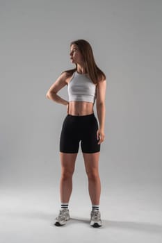 Athletic Caucasian woman in shorts and crop top posing on white background