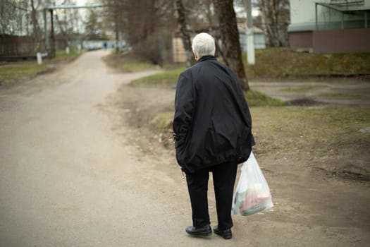 Woman with bag in her hand. Pensioner walks from store down street. Pedestrian on street.