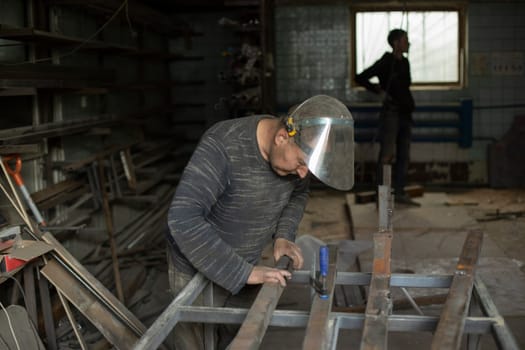 Welder holds metal. People in metal workshop. Work in garage. Worker in protective mask.