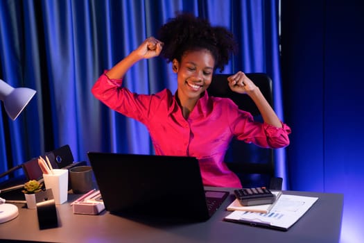 African woman blogger wearing pink shirt with happy face, looking on screen laptop with valued achievement project or get scholarship. Concept of cheerful expression work from home. Tastemaker.