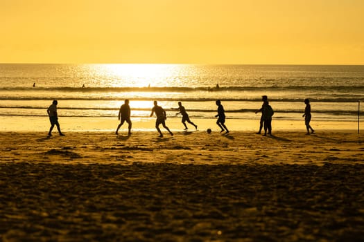 A group of people playing soccer on a beach