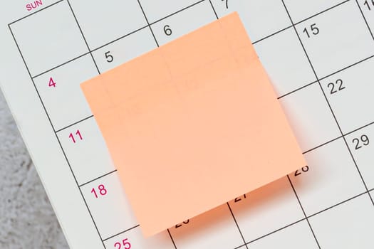 Orange paper sticky note and stuck to a calendar background. Business and reminder concept.