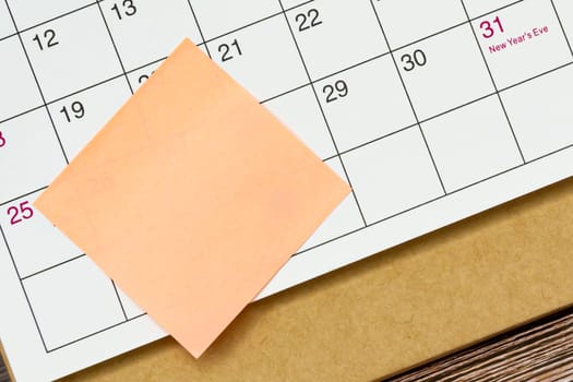 Orange paper sticky note and stuck to a calendar background. Business and reminder concept.