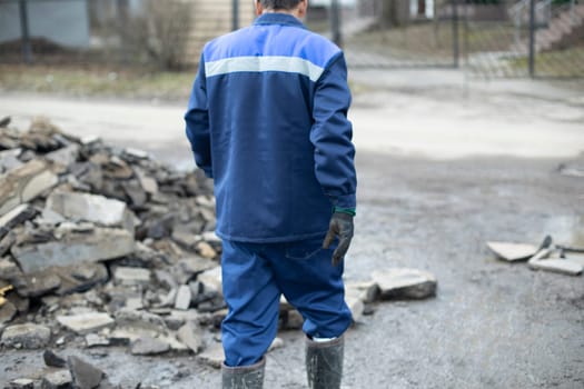 Worker in blue clothes. Road worker removes rocks. Man on construction site.