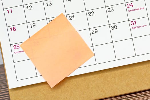 Orange paper sticky note and stuck to a calendar background. Business and reminder concept.