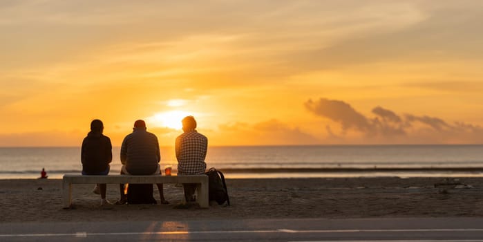 Three people sitting on a bench watching the sun set