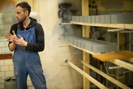 Guy with blue jumpsuit at work. Man in warehouse. Paint shop. Person works. Man rubs his hands.