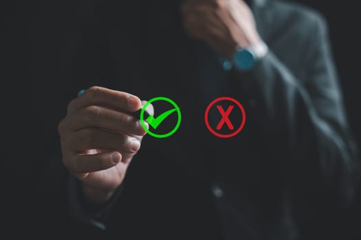 Businessman close-up, in a suit, touches a green checkmark on a virtual screen, pondering yes or no decisions. Evaluation of true and false symbols. Think With Yes Or No Choice.