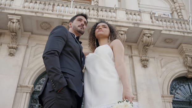 Wedding couples posing on the street. Action. Newlyweds in fashionable wedding costumes posing cute on the street in summer weather. High quality 4k footage