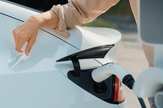 Closeup hand put EV charger to recharge electric car's battery from charging station in city commercial parking lot. Rechargeable EV car for sustainable environmental friendly urban travel. Expedient