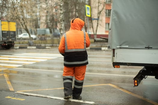 Worker puts cargo in transport. Orange clothes for work. Cleaning road. Man throws bag.