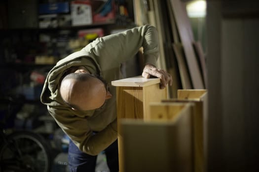 Carpenter makes furniture. Man without hair on his head holds board. Worker makes table out of wood.