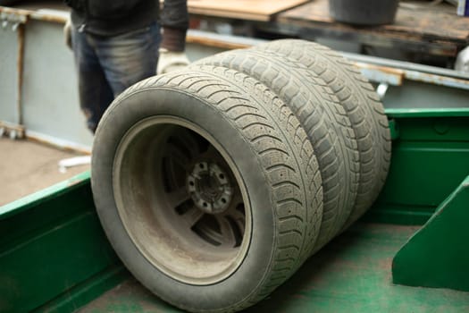 Wheels of car. Replacement of winter tires on transport. Old tires are stacked in trailer. Tire service in city.