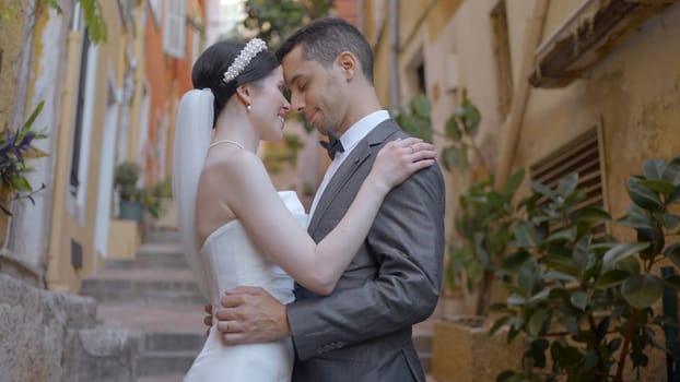 Beautiful couple of newlyweds gently embrace. Action. Beautiful elegant couple in outfits are sexually embracing. Newlyweds in love embrace on stairs of old town.