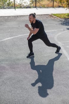 Bearded man with long hair doing lunges on the sports field