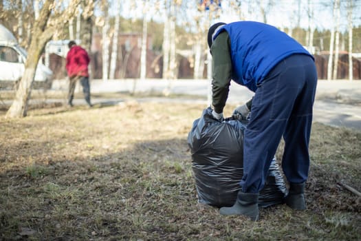 Garbage collection in bag. People clean up yard. Harvesting leaves in park.