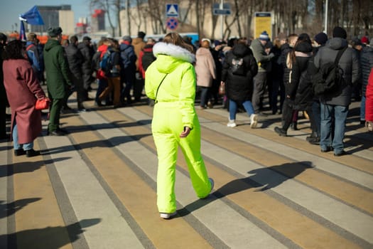Woman in light green cambinison. Bright color of clothes. Alone in crowd. Man in town.