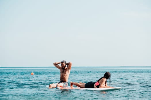 Sea woman and man on sup. Silhouette of happy young woman and man, surfing on SUP board, confident paddling through water surface. Idyllic sunset. Active lifestyle at sea or river