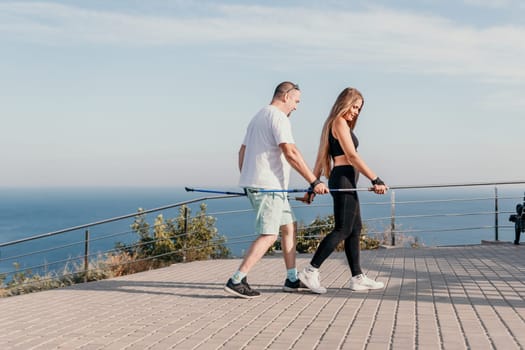 Happy Middle aged couple or friends practicing nordic walking in park near sea. Mature couple with trekking poles walking, practicing Nordic walking outdoors. Aging youthfully and sport concept.