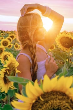 Beautiful middle aged woman looks good in a hat enjoying nature in a field of sunflowers at sunset. Summer. Attractive brunette with long healthy hair