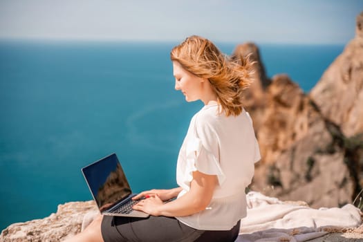 Freelance woman working on a laptop by the sea, typing away on the keyboard while enjoying the beautiful view, highlighting the idea of remote work