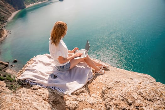 Freelance woman working on a laptop by the sea, typing away on the keyboard while enjoying the beautiful view, highlighting the idea of remote work