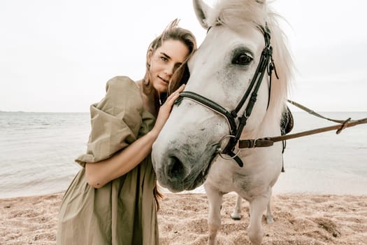 A woman in a dress stands next to a white horse on a beach, with the blue sky and sea in the background