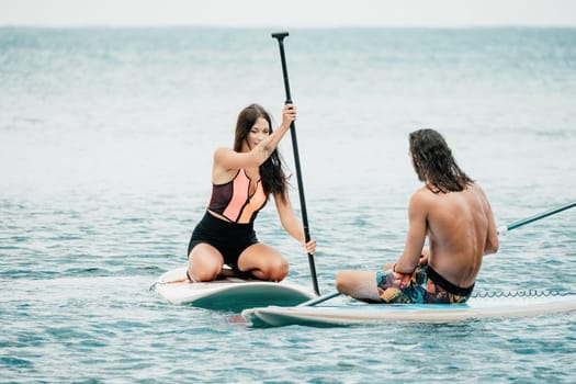 Sea woman and man on sup. Silhouette of happy young woman and man, surfing on SUP board, confident paddling through water surface. Idyllic sunset. Active lifestyle at sea or river