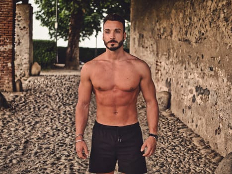 A shirtless man standing in an alley way. Confident Athlete Demonstrating Strength in Front View Portrait