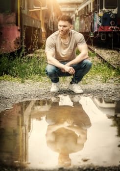 A man sitting on a train track next to a puddle of water. Photo of a man sitting on a train track next to a puddle of water