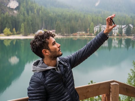 A man is taking a picture of a lake. Photo of a man capturing the scenic beauty of a tranquil lake in the Italian Dolomites