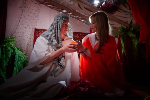 Portrait of young arabian muslim couple in traditional clothes in cozy red room. Fhoto shoot in easten style with male and female model like in harem with a sultan and an odalisque. Partial focus