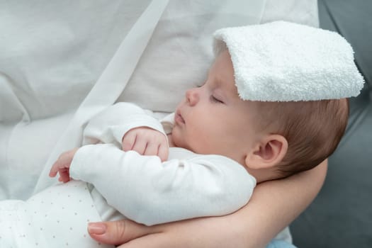 Mother gently places a wet towel on her baby's forehead, aiming to reduce the fever while holding