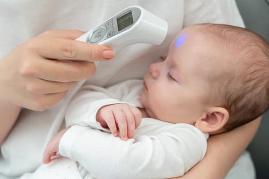 In the frame, a woman focuses on her infant's health, pointing a digital thermometer to the newborn