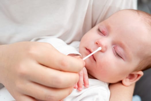 Mother tenderly cleans her baby's nose with a cotton stick, prioritizing comfort and cleanliness