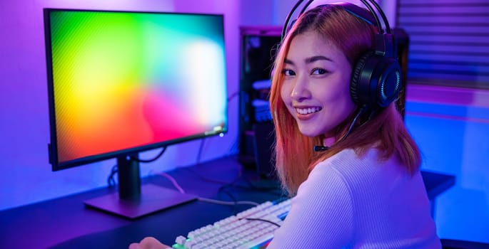 Smiling young woman wearing gaming headphones intend to do playing live stream games online at home looking to camera, Happy Gamer endeavor plays online video games tournament with computer neon light