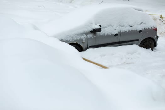 Car in winter in parking lot. Car is parked in snow. Snowdrifts in parking lot. After snowstorm.