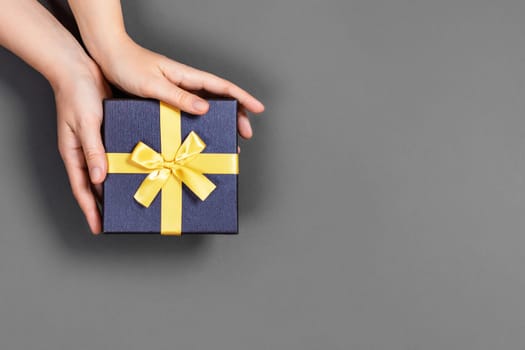 Girl holds gift bandaged with yellow ribbon on gray background. Photo in the colors of the new year.