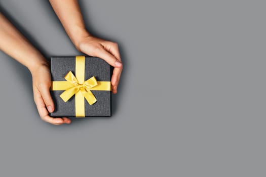 Girl holds gift bandaged with yellow ribbon on gray background.